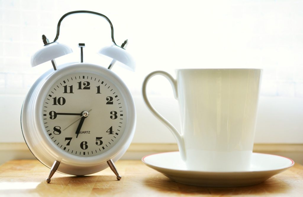 An alarm clock next to a coffee mug.
