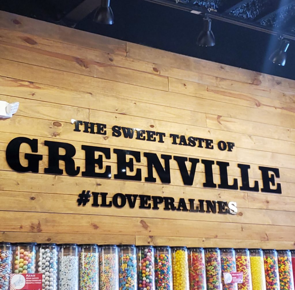 Candy Wall in River Street Sweets, downtown Greenville, SC that says The Sweet Taste of Greenville, hashtag I love pralines